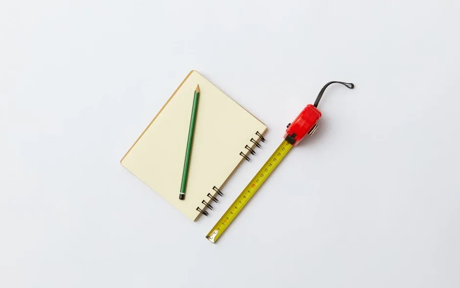 Carnet de notes, crayon et mètre ruban posés à plat sur une table claire